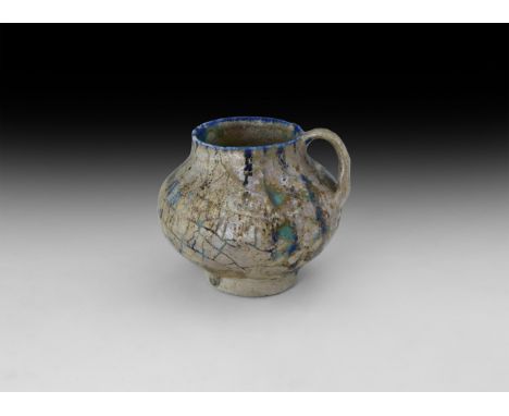 9th-10th century AD. A turquoise glazed ceramic cup with blue trails, bulbous body and short neck, strap handle to the side; 