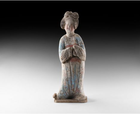 Tang Dynasty, 618-906 AD. A ceramic figure of a courtly lady standing on an irregular base wearing a floor-length gown, one c