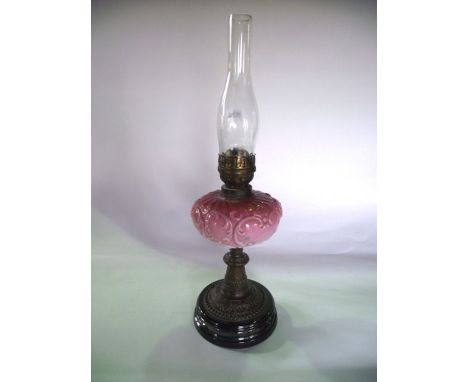 A Victorian oil burning lamp raised on an embossed base accommodating an opaque cranberry shade with scrolling and moulded de