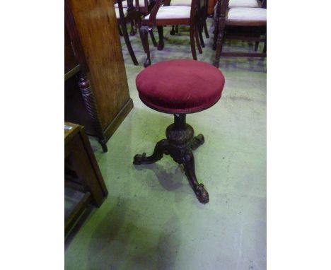 A Victorian walnut piano stool with upholstered revolving adjustable seat raised on turned pillar and scrolled tripod with ca