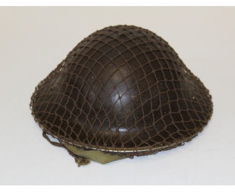 A WWII British Army helmet with leather lining, chin strap and camouflage net
