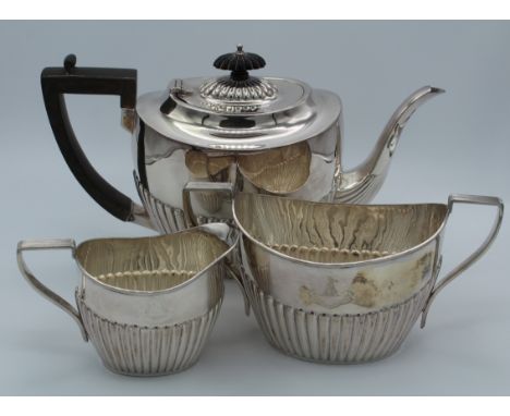 A three piece silver teaset in the George III style with fluted oval bodies comprising teapot, width 29cm, sugar basin, width