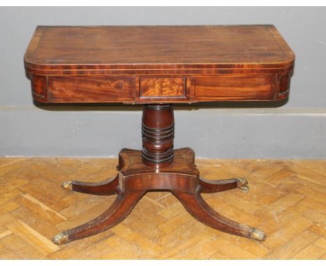 A late George III mahogany, crosbanded and line inlaid card table, raised on a turned column and quadruple splay legs, damage