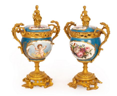A pair of Sèvres style cups and covers, the blue ground with vignettes of putto and flowers, with gilt metal mounts and finia