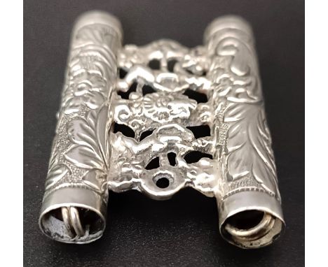 An unusual silver coloured metal hat toggle, decorated figures, 17.8 g