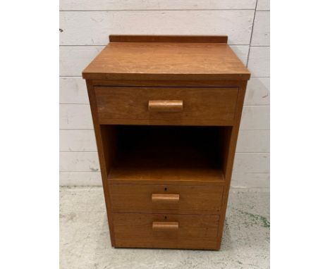A teak three drawer bedside table with central shelf and on castors (H78cm W47cm D43cm)