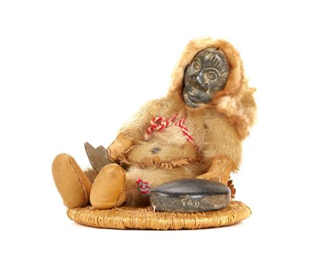 Annie Tooktoo Inuit doll or figure with a carved stone face and fur garments. The figure rests on a basket woven base.Height: