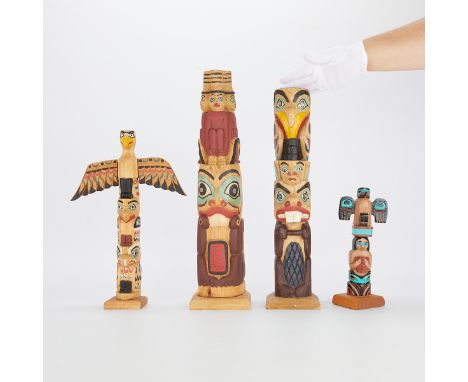 Group of four carved and hand painted totem poles. The shortest totem pole with "Raven / Sun, Moon, Stars in Box / Chief / Sa