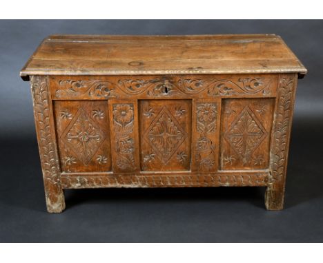 An early 18th century oak blanket chest, hinged rectangular top, three panel front carved with lozenges, flowers and leafy sc