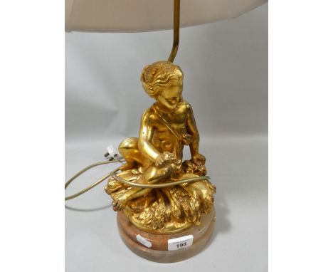 A table lamp in the form of a gilt cherub seated on a marble base with beige shade. 65cm tall. 