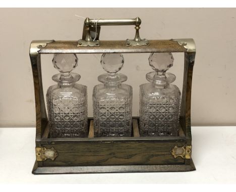 An Edwardian oak and silver plate mounted three bottle Tantalus  CONDITION REPORT: Small losses to each corner of base. 33cm 