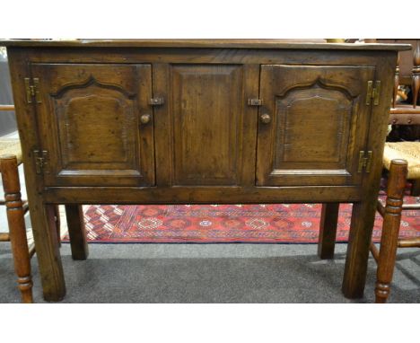 A small 17th Century style oak cupboard centred by a panel flanked by a pair of fielded panelled doors on moulded block legs,