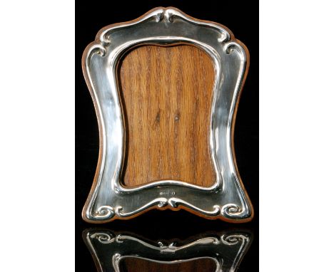 A modern silver mounted wooden easel back photograph frame of shaped outline in the Art Nouveau style, with scrolled border e