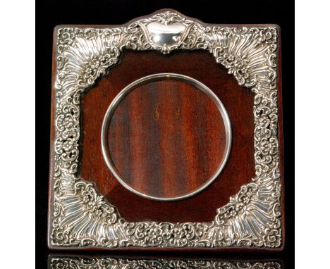 An Edwardian hallmarked silver mounted easel back photograph frame, the circular aperture within a square wooden frame, scrol