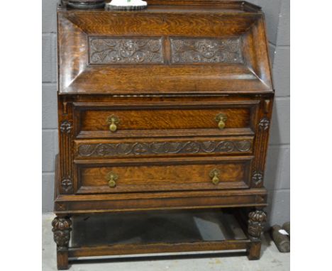 A 1920s carved oak bureau the gallery back over a carved fruiting panel fall and fitted interior above two long drawers on tu