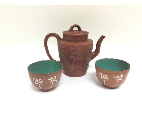 A terracotta teapot with applied decoration depicting a peacock and a pair of terracotta tea bowls (3). Shipping category D.