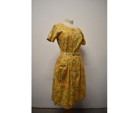 A 1950s floral day dress in yellow hues, with original belt, heart shaped patch pocket to front and button fastening.
