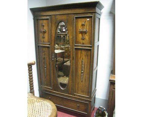 A 1920's Oak Wardrobe, with a central oval mirror, panelled sides, with applied decoration, base with single drawer on stile 