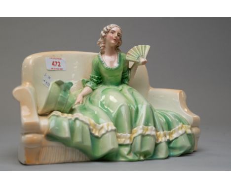 A katzhutte figurine of lady on sofa holding a fan with bonnet by her side in green and yellow period costume, approx 27cm wi