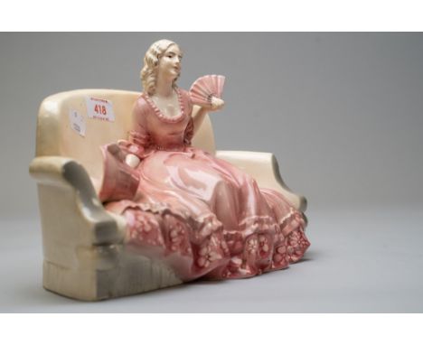 A katzhutte figurine of lady on sofa holding a fan with bonnet by her side in a pink period costume, approx 27cm wide by 18cm