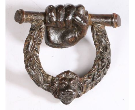 A 19th century cast iron door knocker, circa 1820Designed as a clenched fist holding a bar, with laurel-leaf lion mask centre