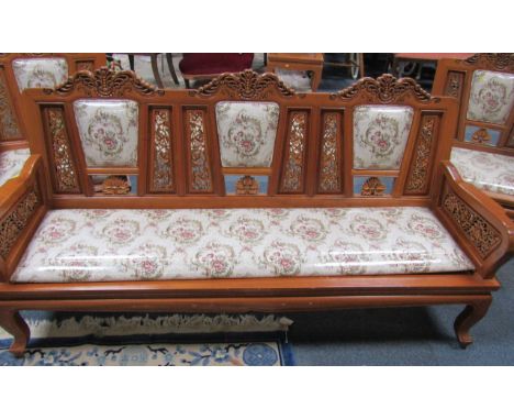 An Indonesian carved hardwood lounge suite, comprising two three seater settees, with carved pierced and padded backs with fl