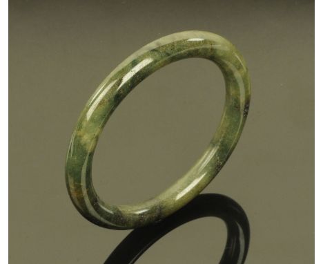 A Chinese polished jade bangle, 20th century, of mottled green colour with natural inclusions, interior diameter 5.2 cm.