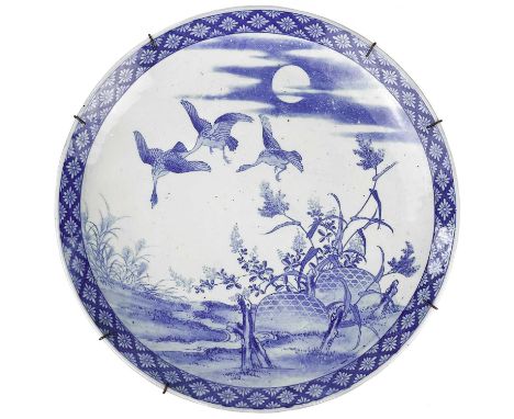 A Japanese blue and white porcelain charger, Meiji period. Decorated with birds in flight above a landscape with trees and st