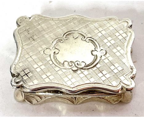 A Victorian silver vinaigrette of typical form with wavy edges, engine-turned decoration around a cartouche, the hinged lid o