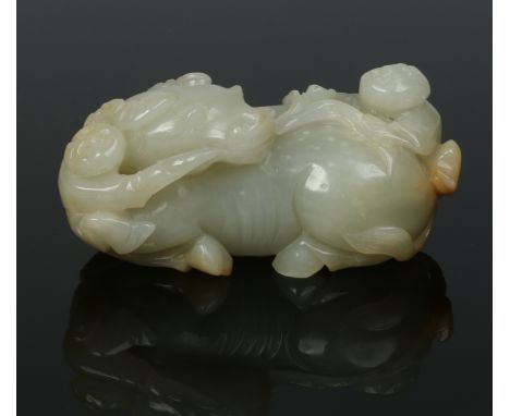 A Chinese Qing dynasty carved celadon jade model of a recumbent buffalo. Holding a branch in its mouth with its head turned t