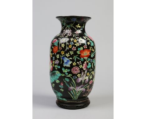 A 20th century Chinese famille noir vase painted in coloured enamels with flowers and raised on a hardwood plinth. Printed Da