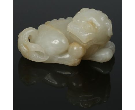 A Chinese Qing dynasty celadon jade carving of a recumbent temple dog guarding a ball. Modelled in a slightly curled pose wit
