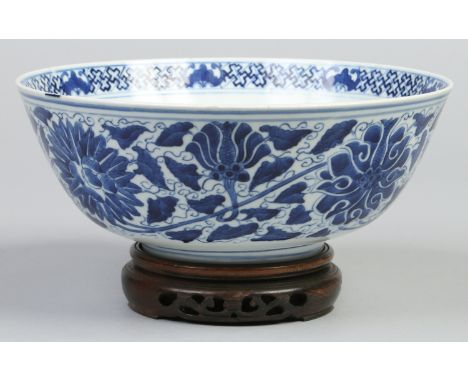 A Chinese Kangxi style bowl on hardwood stand, painted in underglaze blue with a band of stylized leaves and flowers, with an