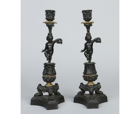 Two bronzed metal candlesticks in the Classical style, the pedestals formed as putti and raised on triform bases with claw fe