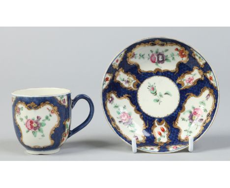 A Worcester scale blue ground coffee cup and saucer. With gilt cartouches containing enamelled European flowers. Crescent mar