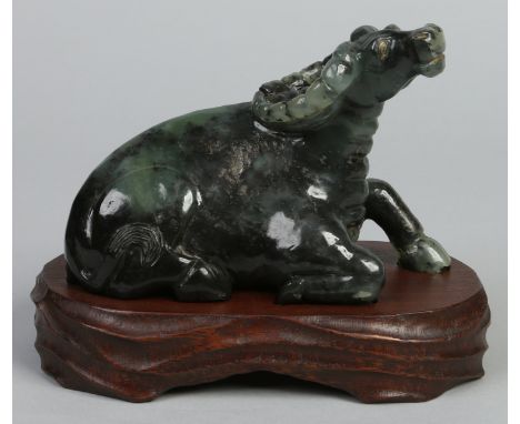 A Chinese mottled spinach jade coloured hardstone carving of a recumbent water buffalo raised on a carved hardwood plinth, 23