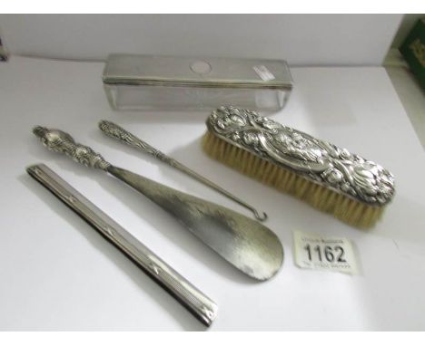 A silver lidded trinket box, a silver backed brush, a silver handled button hook, a silver handled shoe horn and a silver com