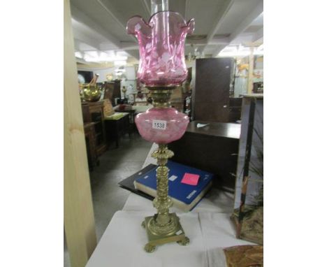 A brass oil lamp with etched cranberry font and shade.