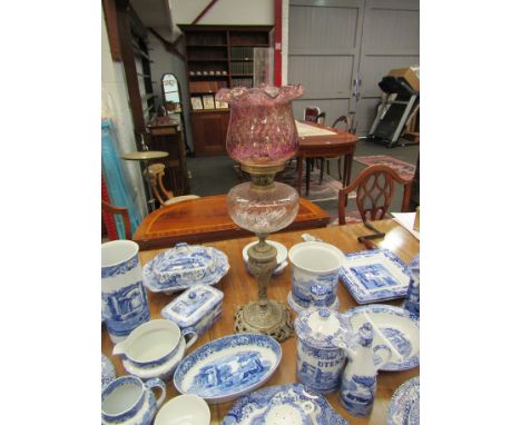 An oil lamp with frilled cranberry glass shade on ornate brass base