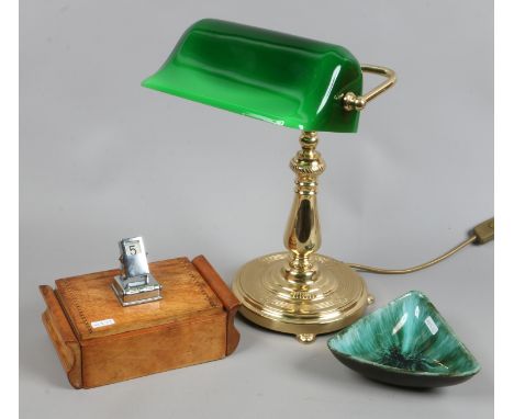 A brass based desk lamp, along with a desk calender/cigarette dispenser and a blue mountain pottery dish.