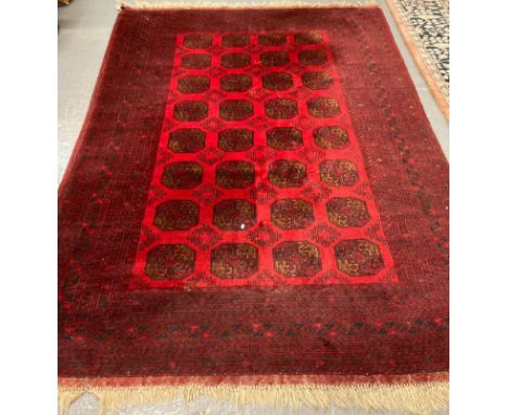 Middle Eastern design red ground carpet with a collection of central geometric medallions flanked by stylised floral borders.