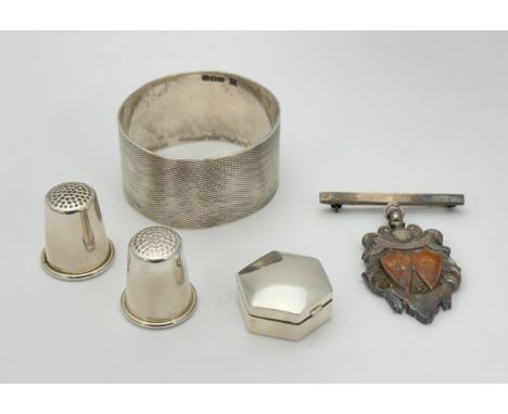 A small hexagonal silver pill box, two silver thimbles, a silver napkin ring and a fob medal