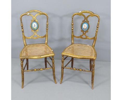 A Pair of antique salon chairs, with gilded finish, featuring cane seats and hand painted ceramic figural back panels.Cane in