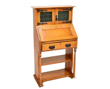 An Arts &amp; Crafts oak bureau bookcase of small proportions, the twin cupboard doors with green and leaded glazed panels ab