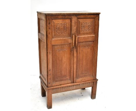 ALAN BROUGH (1890-1986): an adzed oak cabinet, the twin panelled doors with carved foliate and linen fold detail enclosing tw