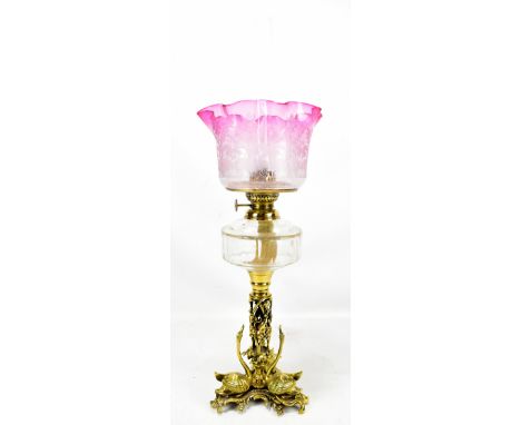 A Victorian brass oil lamp with cranberry glass shade above clear glass reservoir and pierced brass base, the column with thr