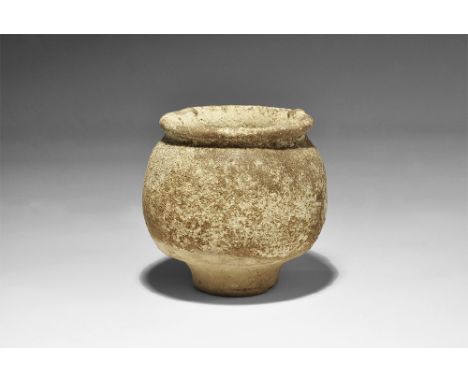 1st millennium BC. A squat ceramic jar with discoid narrow base, bulbous body and flared rim with three radiating lugs, added
