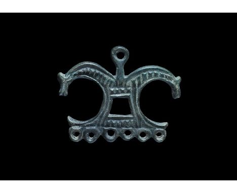 11th-12th century AD. A bronze bifacial pendant formed as two addorsed horse-heads springing from a plaque with central trape