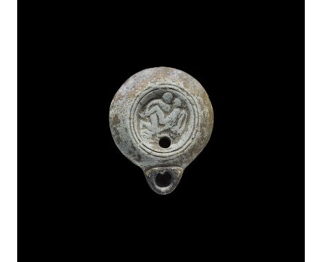 1st century AD. A carinated discoid ceramic oil lamp with short nozzle, basal ring; to the discus, a reserved scene of two lo
