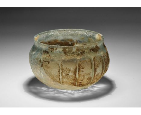 3rd-4th century AD. A pale blue glass bowl with iridescent surface, flat bottom, vertical ribbed segmentation, slightly evert